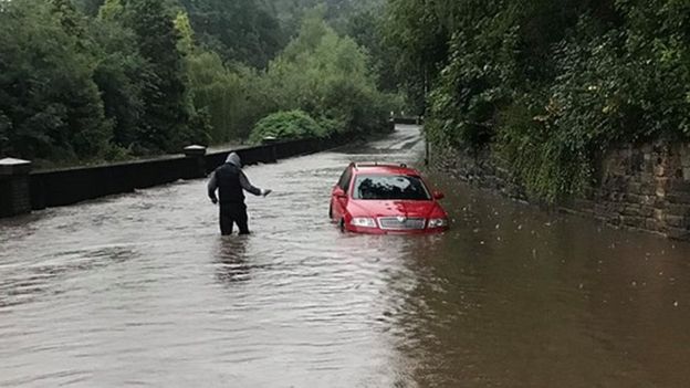 Man wades through water as car stuck in flooded road