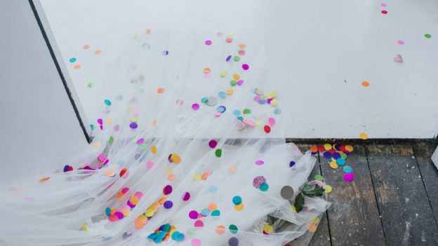 Bride leaves her ceremony with the train of her dress covered in coloured confetti