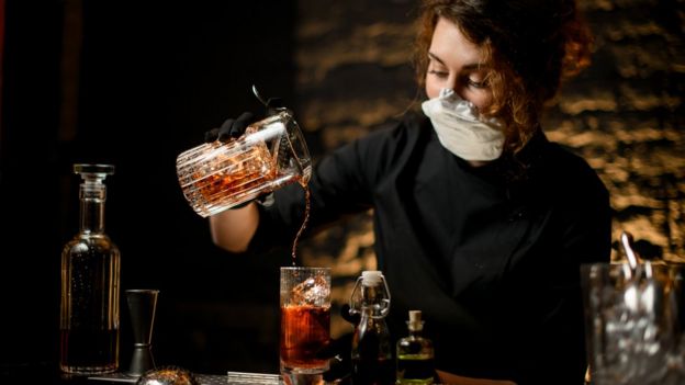 A bartender pouring a drink, wearing a mask