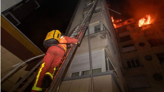 This handout picture taken and released by the Paris firefighters brigade in the night of February 5, 2019 shows a fireman climbing up a ladder as a fire burns in a building in Erlanger street in the 16th arrondissement in Paris