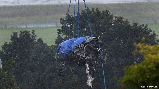 The damaged remains of the fuselage of a Hawker Hunter fighter jet are lifted by crane
