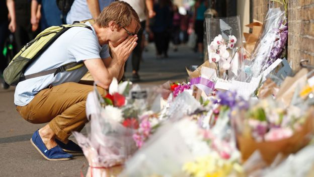 Joven mostrando consternación frente a flores dejadas por el público tras el ataque