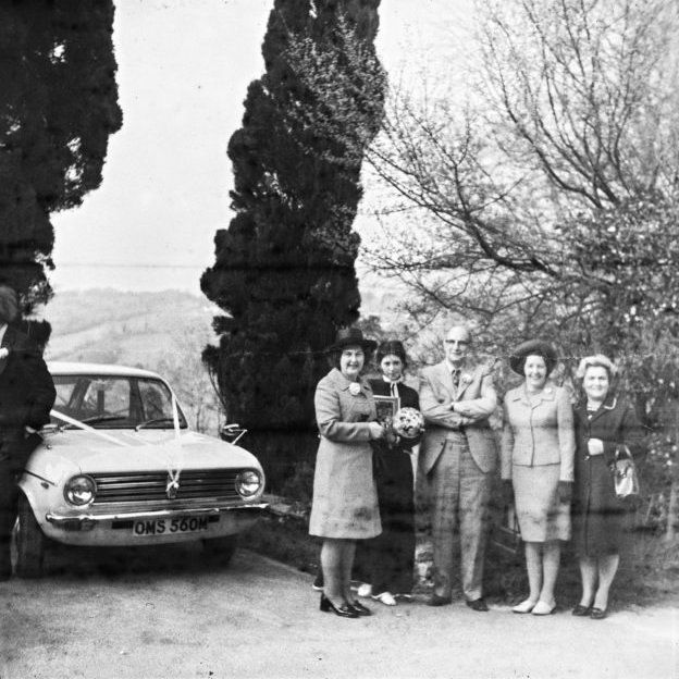 Black and white photo of wedding guests and car