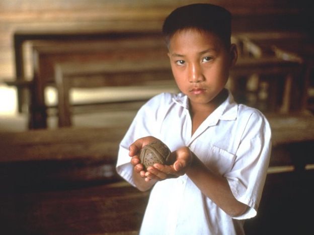 Un niño de Laos muestra una bomba de racimo