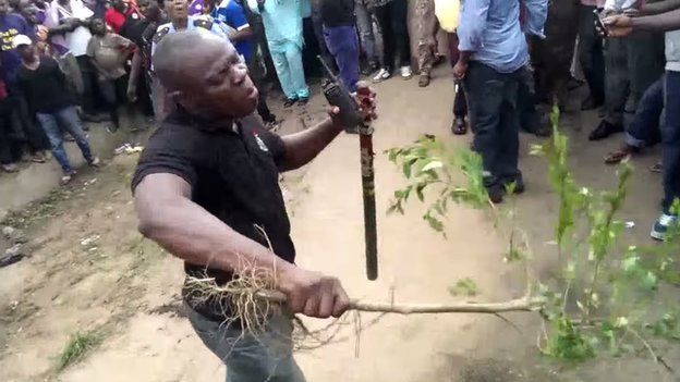 A man beating a crowd back with a branch