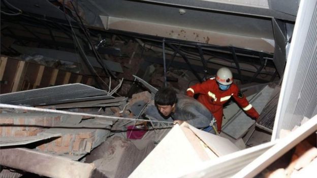 A rescuer follows an injured man walking out of the rubbles of a collapsed five-story hotel building in Quanzhou city in southeast China's Fujian province, 7 March 2020