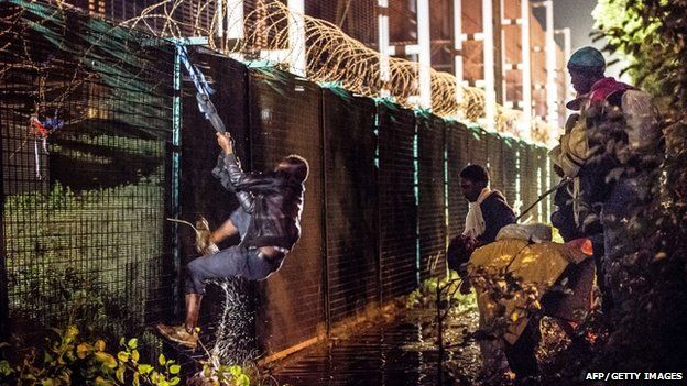 A migrant climbs a security fence at Calais