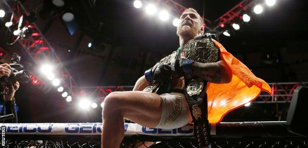Conor McGregor celebrates with his two championship belts after defeating Eddie Alvarez