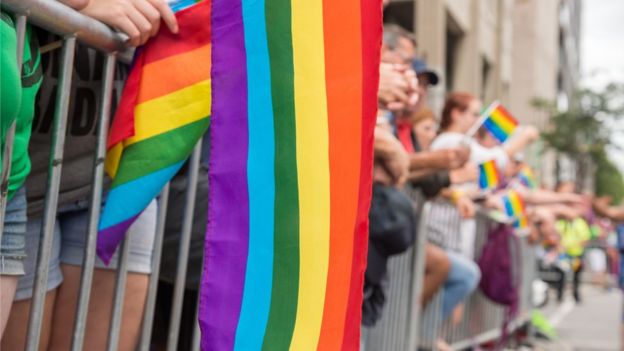 Pessoas com bandeira do arco-íris na mão em parada LGBT