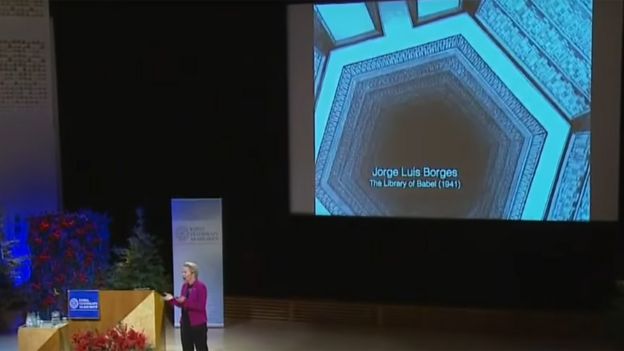 Arnold durante su discurso en Suecia con una ilustración que hace referencia a La Biblioteca de Babel en el fondo
