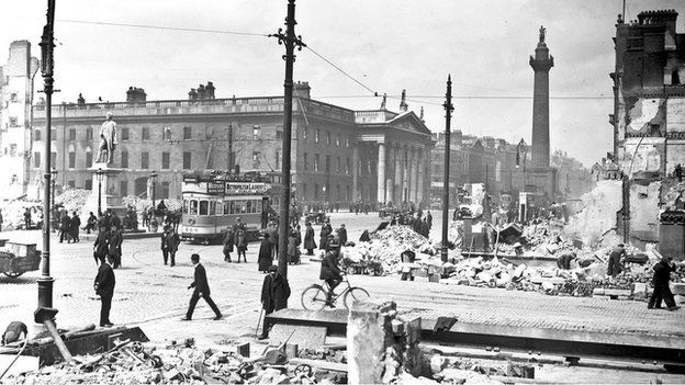 Crowds in O'Connell Street can be seen next to the General Post Office showing damage from shelling following the Easter Uprising
