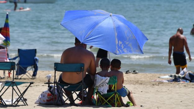 People sit under an umbrella at a beach in France in June