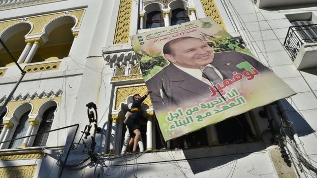 Algerian demonstrators tear down a large billboard with a picture of former President Abdelaziz Bouteflika.