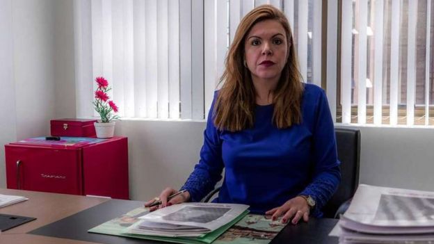 A promotora Andressa Lanchotti olha para a câmera sentada em sua mesa de escritório