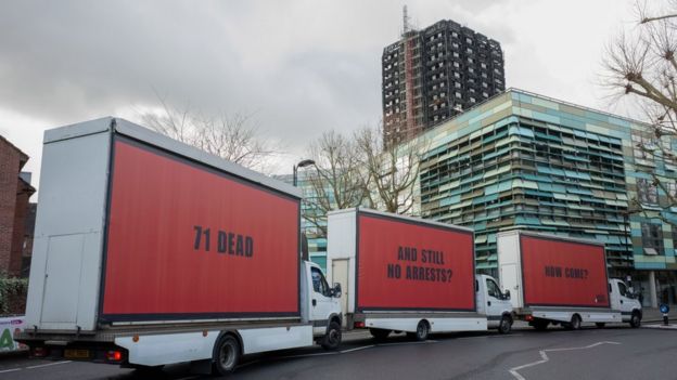 Three vans bearing billboards parked in Kensington with the fire-damaged Grenfell Tower in the background