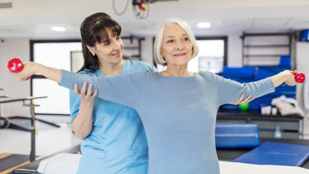 Una mujer mayor realiza un ejercicio con pesas bajo supervisión de una entrenadora