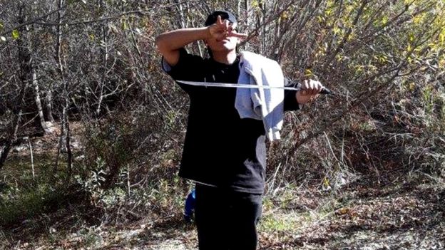 Un joven señalado como uno de los sospechosos de los delitos sostiene un machete y hace una señal con la mano característica de la MS-13