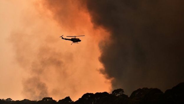 A helicopter flies near black smoke from a bushfire