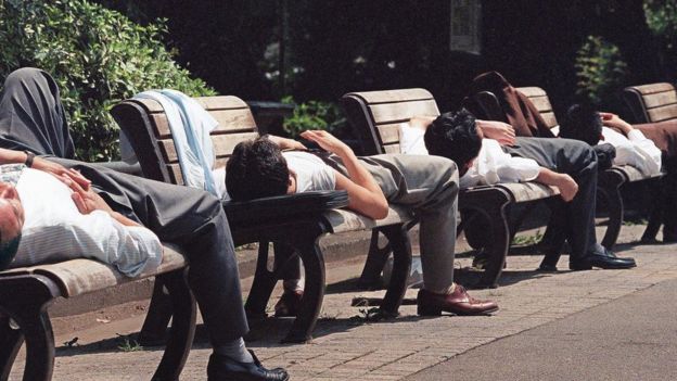 Homems pegam sol deitados em bancos no Japão, onde chegam a ocorrer mortes por trabalho excessivo