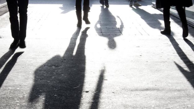 أشخاص يسيرون في الشارع ويبدو ظلهم واضحا أمامهم