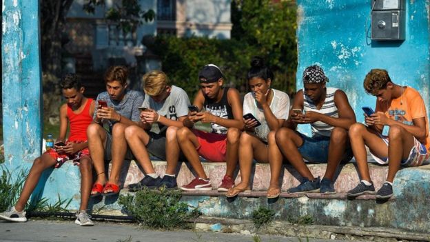 Jovens sentados na rua mexendo nos seus celulares