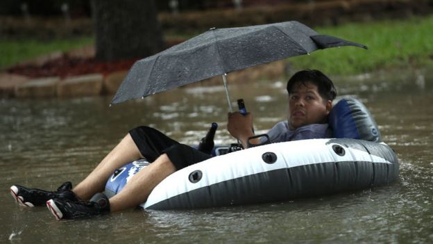 Un hombre bajo un paraguas y a bordo de una lancha huye en una calle inundada de Houston.