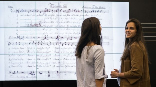 Jovens em frente à letra em exibição no museu de Salzburgo