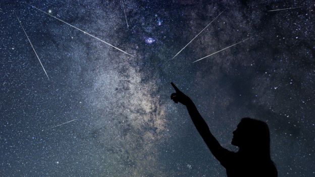 Mujer apuntando a estrellas fugaces en el cielo