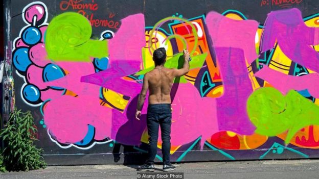 Homem fazendo grafite em muro