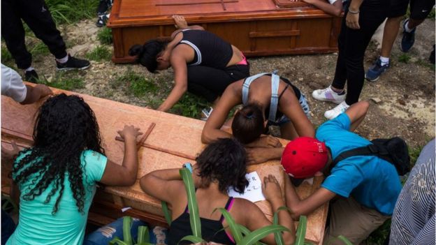 Pessoas debruçadas sobre caixão em um enterro