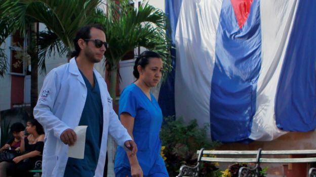 Dois profissionais de saúde caminham em frente a uma bandeira cubana no hospital Calixto Garcia, em Havana