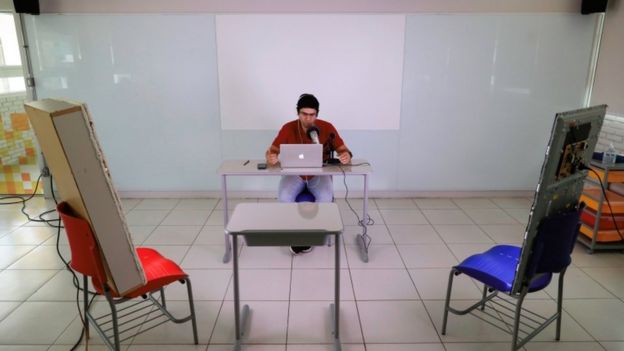 O professor Fabiano da Silva em sala vazia, em frente a laptop e falando no microfone para alunos