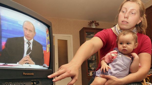 Una mujer con un menor en el regazo observa a Putin en la televisión