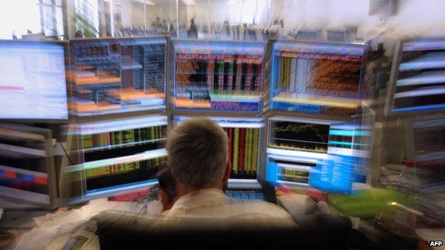 Stock market trader on the phone in front of screens with blurred financial readouts