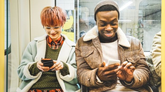 Una pareja de jóvenes mira su celular en el metro.