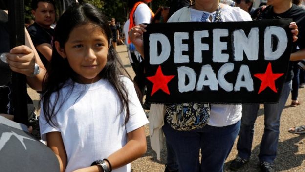 Child stands in front of a 'Defend Daca' sign