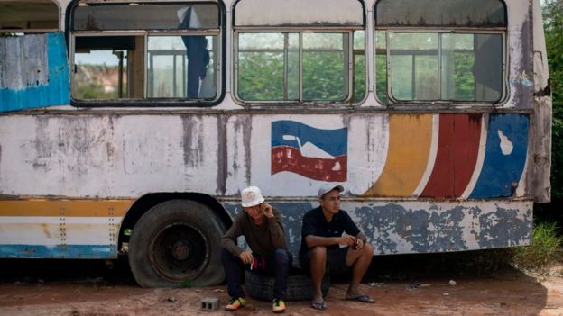 Dois venezuelanos sentados em frente a ônibus deteriorado em Roraima