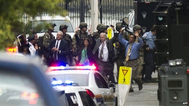 People exit a building with their hands above their heads as police respond to the report of a shooting at the Washington Navy Yard on 16 September 2013