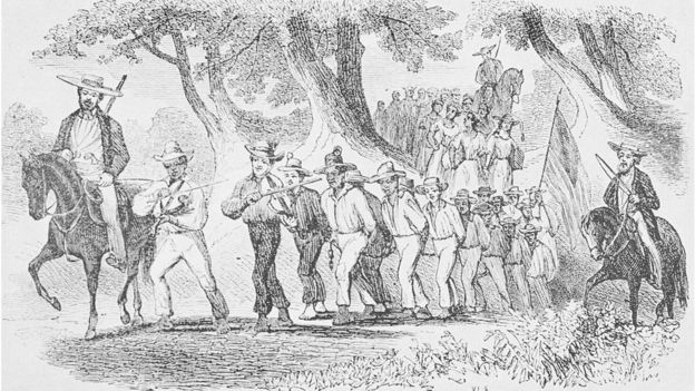 An etching depicting a group of slaves being marched while they are bound together with chains, they are being led by white men on horses who carry guns and whips