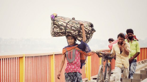 A woman walking, carrying a big bag on her head