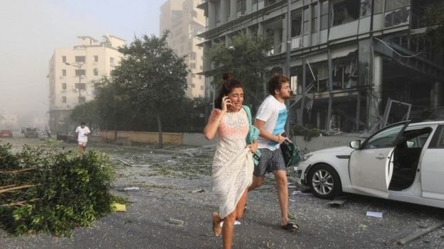 Dos personas huyen del área después de la explosión en el puerto de Beirut.