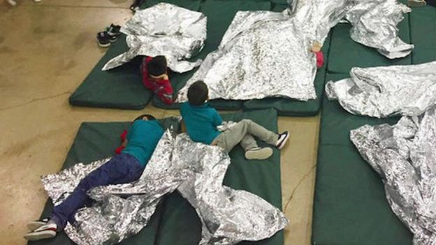 Three boys lie on thin green mattresses on the floor covered in foil blankets