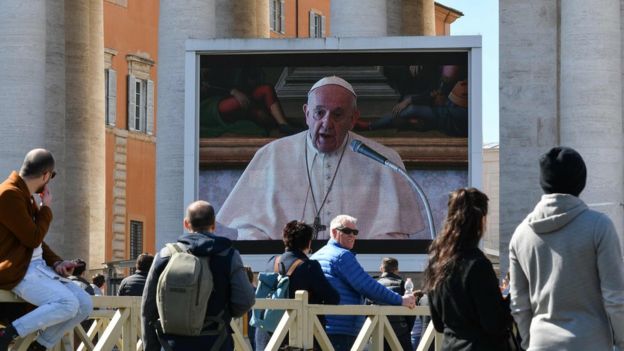 {eople watch a screen live-broadcasting Pope Francis's Sunday Angelus prayer in St. Peter' s Square at the Vatican