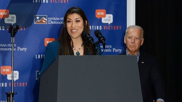 Lucy Flores hablando en 2014, durante un evento de campaña en Nevada con Joe Biden detrás de ella