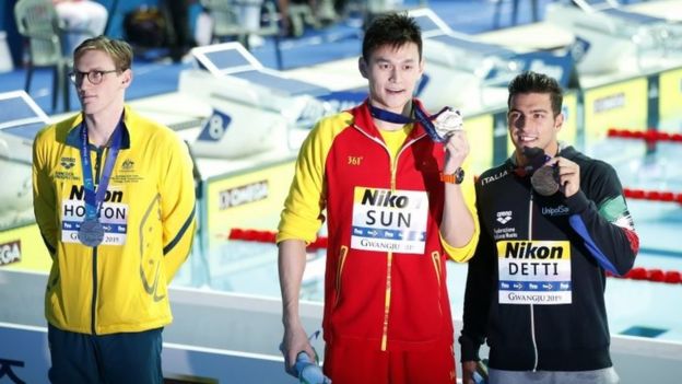 Mack Horton stands in the background as Sun Yang and Gabriele Detti pose for photos with their medals