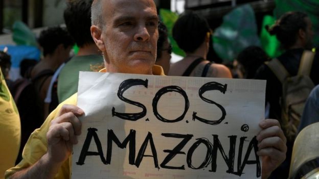 A man holding a sign saying "SOS Amazonia"