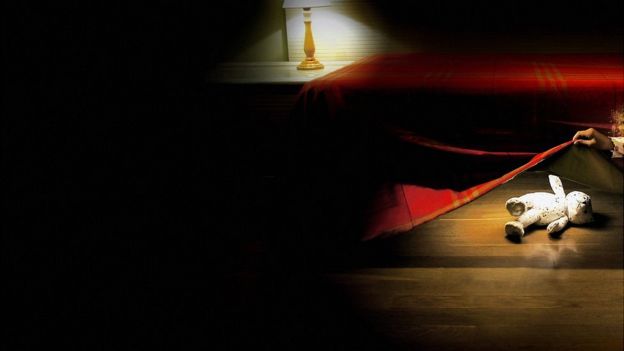 Imagem mostra o ambiente de um quato, com uma luminária acesa, um bicho de pelúcia e alguém olhando debaixo da cama