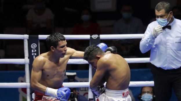 Boxeadores en el ring, el juez lleva una mascarilla