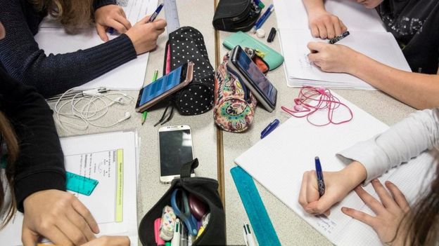 Alunos em sala de aula com celulares sobre a mesa