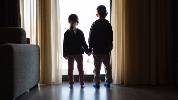 Duas crianças em isolamento, dentro de casa, olhando para a janela